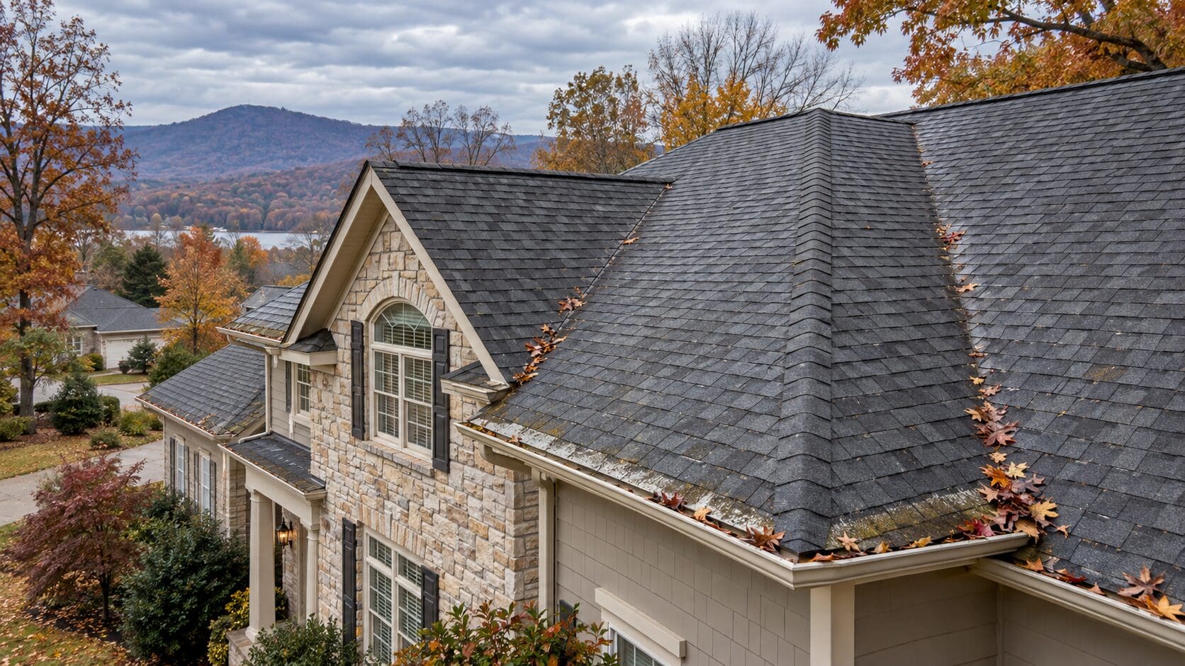 Huntsville AL home with an asphalt shingle roof in late fall showing light leaf debris, faint granule loss, damp shaded areas, and minor roof-edge staining after rain.